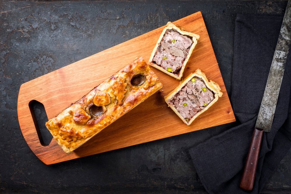Une tourte à la viande enceinte sur une planche à découper avec un couteau.