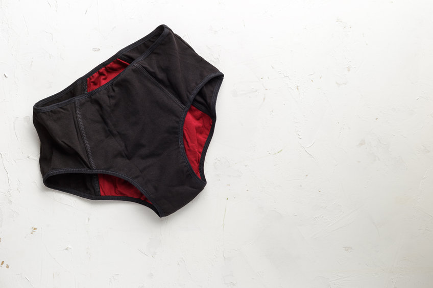 Une paire de sous-vêtements taille haute noirs et marron conçus pour la protection menstruelle est posée à plat sur une surface de couleur claire.