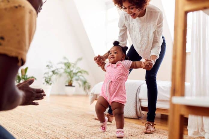 Un enfant apprentissage de la marche est encouragé par ses parents dans un salon.