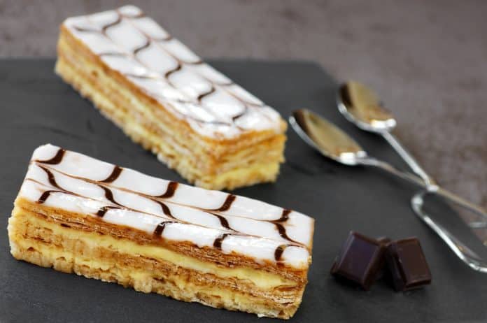 Deux desserts mille-feuille d'enceinte sur une assiette avec des cuillères à côté d'eux.