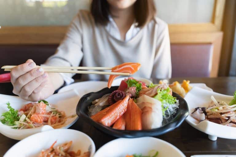 Une femme, démontrant son savoir-faire en matière de sushis, tient des baguettes devant un bol de nourriture asiatique.