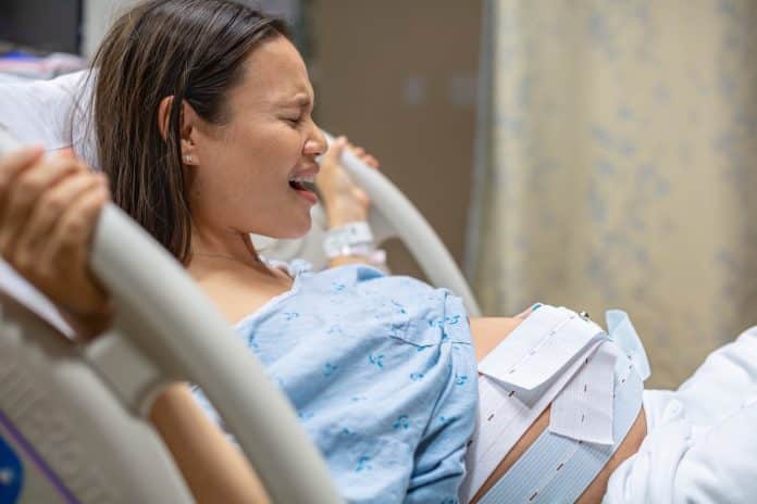 Une femme enceinte est allongée dans un lit d'hôpital, souffrant de la phase de latence avant l'accouchement.