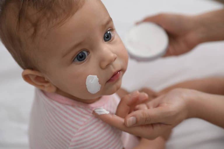 Un bébé se fait appliquer une crème sur le visage.