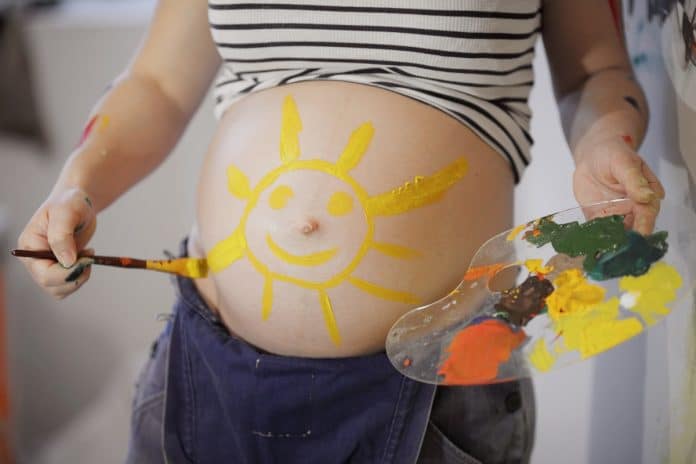 Une femme enceinte peignant un soleil sur son ventre.