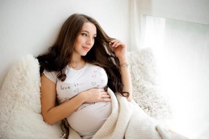 Une femme enceinte allongée sur un canapé avec une couverture, mettant en valeur ses cheveux radieux.