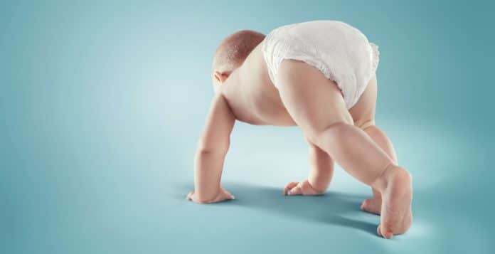 Bébé à la peau sensible rampant dans une couche sur fond bleu.