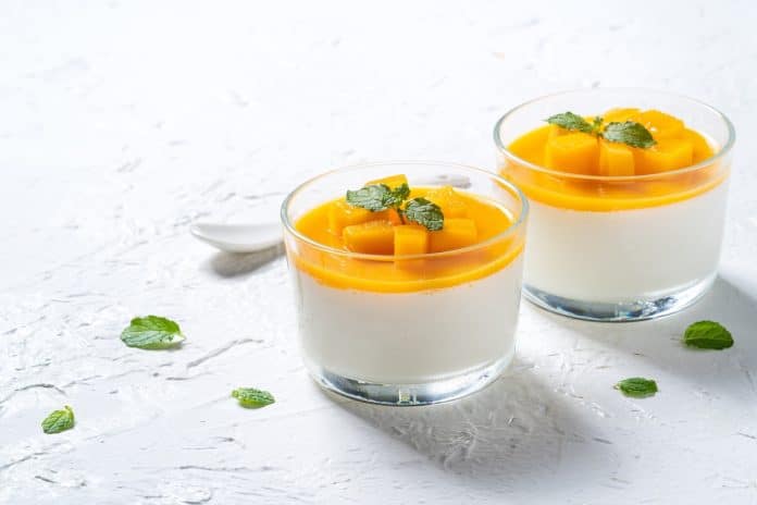 Deux verres de panna cotta à la mangue garnis de feuilles de menthe sur une surface blanche texturée, parfaits pour les femmes enceintes.