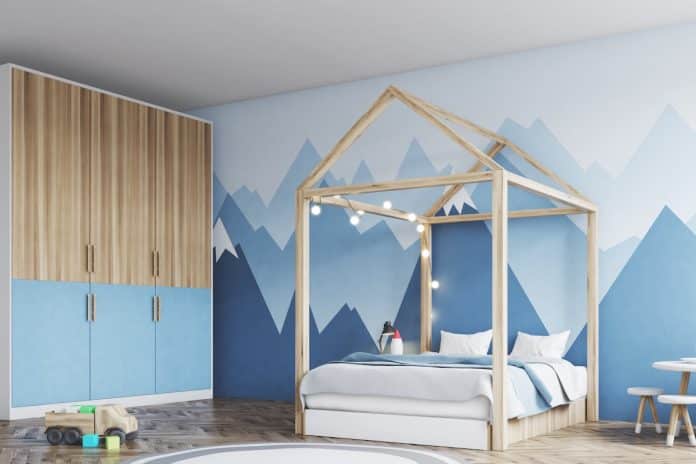 Une chambre d'enfant comprenant un cadre de lit double en forme de maison avec des guirlandes lumineuses, une fresque murale de montagne au mur et des meubles en bois.