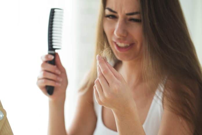 Une femme, après l'accouchement, tient un peigne dans une main et regarde les mèches de cheveux dans l'autre, semblant inquiète de la chute des cheveux.