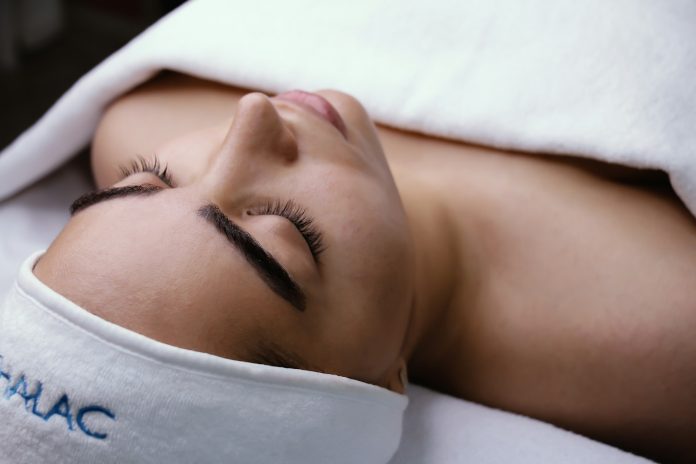 Une personne portant un bandeau et recouverte d'une serviette blanche est allongée, les yeux fermés, et profite d'une cure thermale qui favorise la régénération cellulaire, souvent plus efficace pendant le pic de régénération de 23h à 2h.