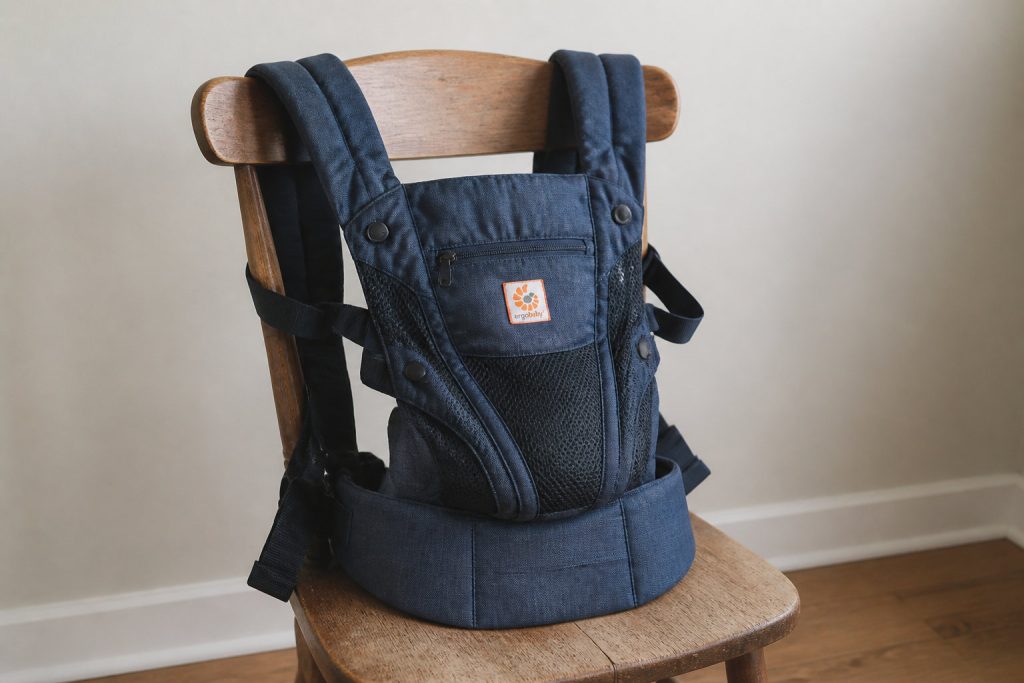 Un meilleur porte-bébé bleu avec des accents en maille noire, idéal pour le confort et le soutien, est présenté sur une chaise en bois contre un mur beige uni - parfait pour votre sélection 2026 d'options de porte-bébé physiologique.
